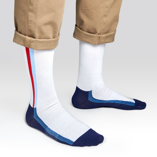 A person wearing tan pants with cuffs, showing white crew socks featuring blue toes, heels, and side stripes, plus a single red stripe on the outer sides.