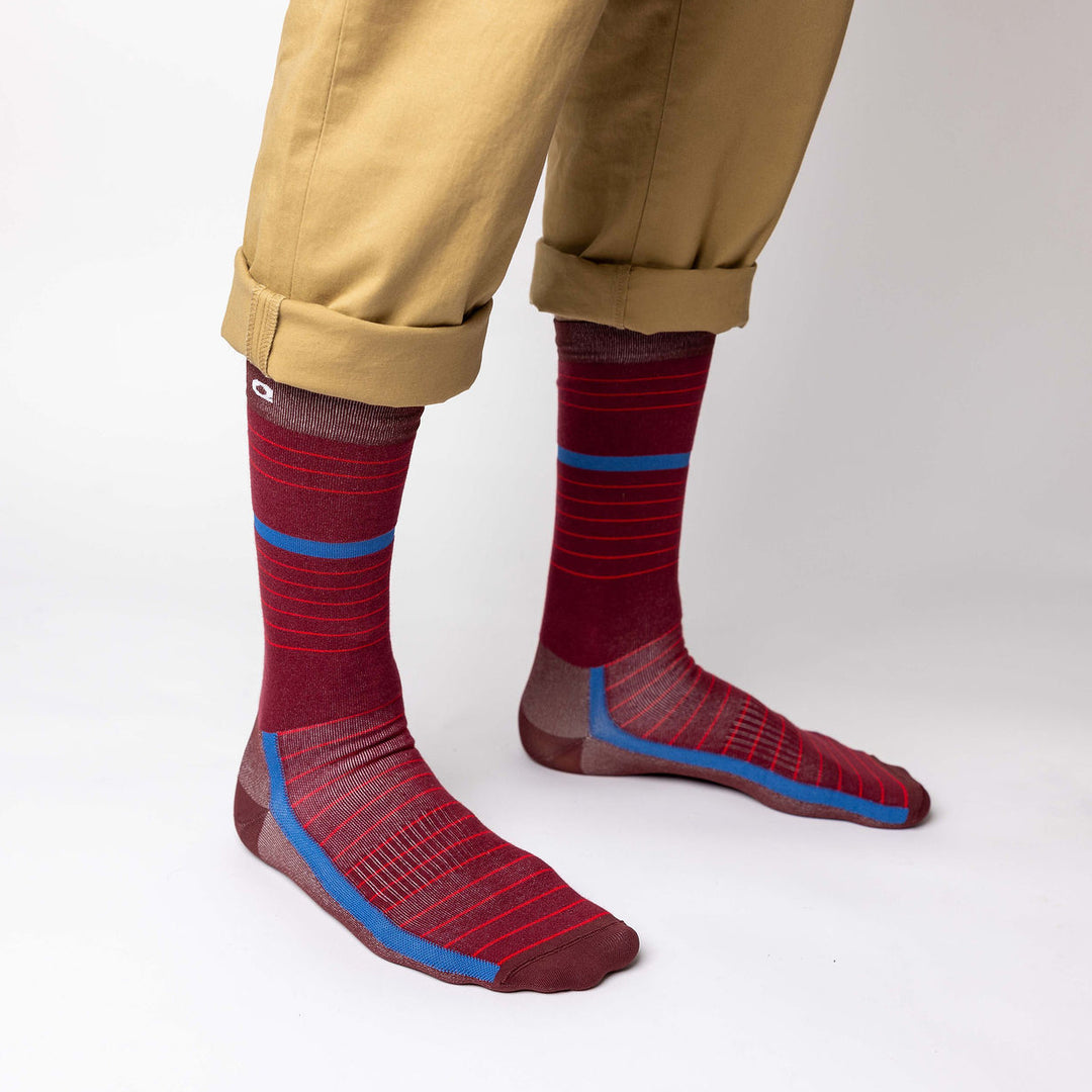 A person wearing tan pants with rolled cuffs and burgundy socks featuring red stripes and blue accents, standing on a white background.