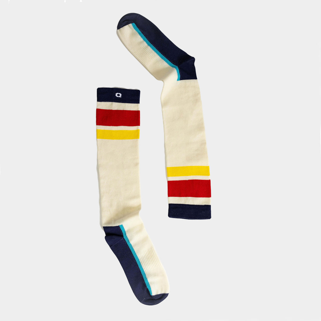 A pair of cream-colored knee-high socks with navy toes, heels, and cuffs, featuring horizontal red, yellow, and navy stripes near the top and bottom. The socks are laid flat on a white background.