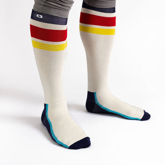 Person wearing long cream-colored socks with red and yellow stripes near the top, navy toes and heels, and light blue accents, standing on a white background.