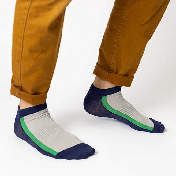Person wearing mustard-colored pants and low-cut socks with navy blue toes and heels, gray tops, and a green stripe, standing on a white background.