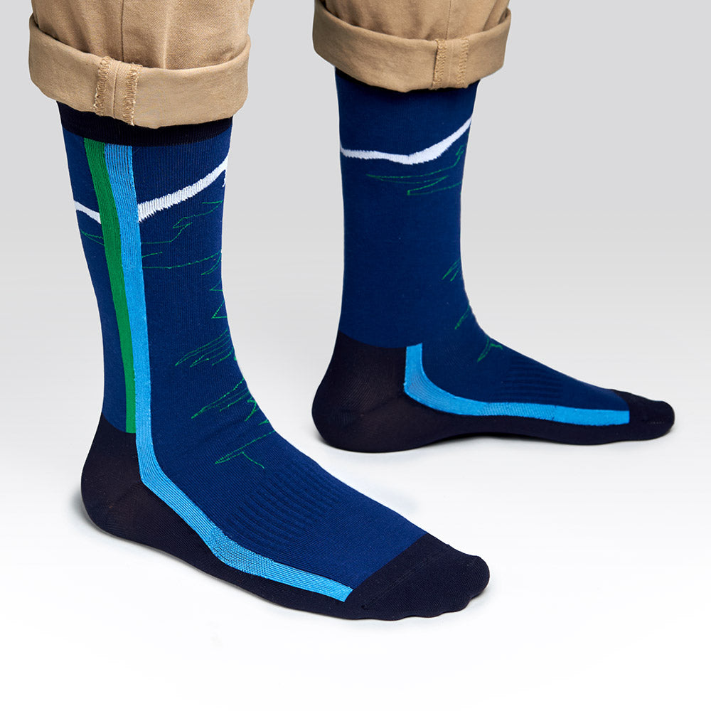 A person wearing cuffed khaki pants and blue socks with green, blue, and white geometric patterns stands on a light gray background.